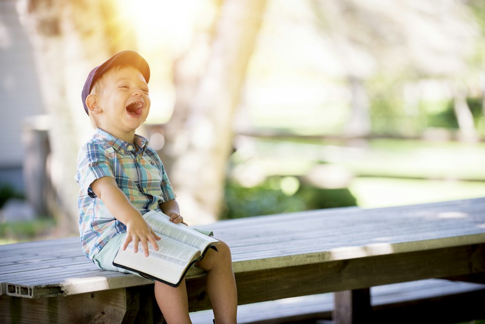Laughing toddler with a book on an outdoor bench